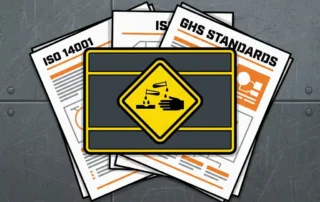 Geel ruitvormig bijtend-stofbord op industrieel etiket, omringd door internationale compliance-documenten op stalen werkoppervlak.